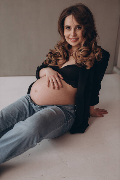 Молодая красивая роскошная беременная женщина позирует на твердом фоне и показывает свой живот  - Фото, изображение