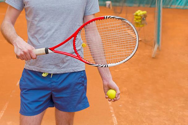 Tennis player holding racket and yellow ball on the orange tennis court - Foto, Imagem