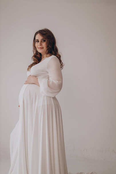 Mladá krásná luxusní těhotná žena pózuje na pevném pozadí a ukazuje své břicho  - Fotografie, Obrázek