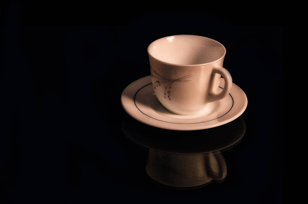 Ένα φλυτζάνι με λευκό πιάτο που απομονώνονται σε ένα μαύρο φόντο με αντανάκλαση. - Φωτογραφία, εικόνα