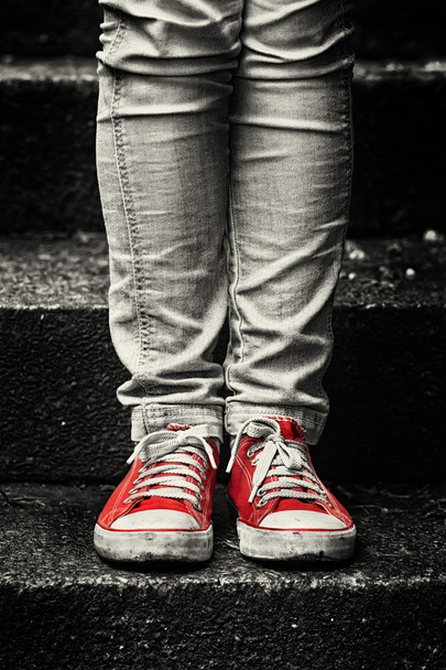 κοριτσάκι σε κόκκινο πάνινα παπούτσια και τζιν μόνιμης στις σκάλες - Φωτογραφία, εικόνα