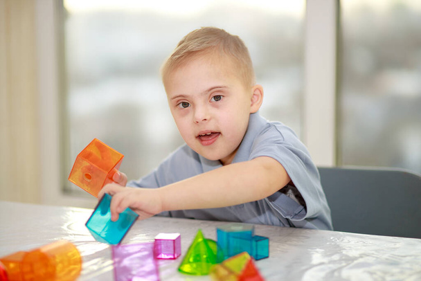 Een jongen met het syndroom van Down speelt met geometrische figuren, een plastic constructeur, type 21 trisonomie, een extra chromosoom. - Foto, afbeelding
