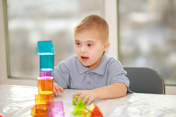 Un niño con síndrome de Down juega con figuras geométricas, un constructor plástico, trisonomía tipo 21, un cromosoma extra. - Foto, imagen