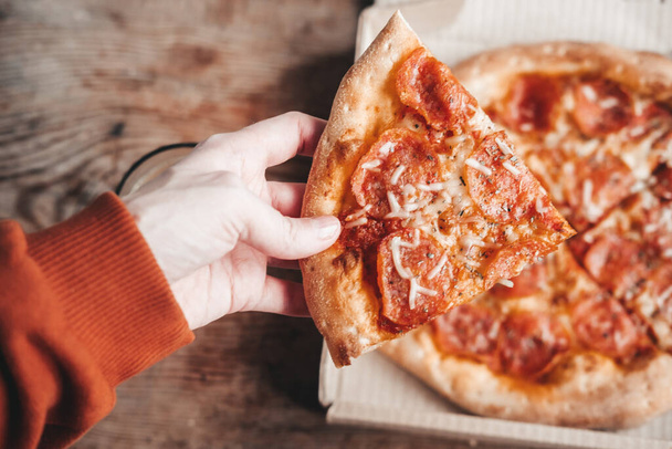 large slice of pepperoni pizza in hands, close-up. Delicious Italian snack. Pizza with salami. - Foto, Bild