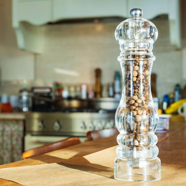 Beautiful glass pepper shaker stands on a wodden table on kitchen background. Food concepts. - Foto, Imagem