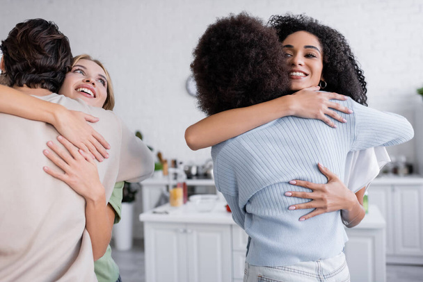 happy interracial friends hugging in modern apartment - Photo, Image