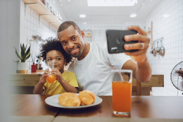 Feliz afroamericano Fther y niño pequeño tomando selfie con teléfono inteligente en casa juntos. - Foto, imagen
