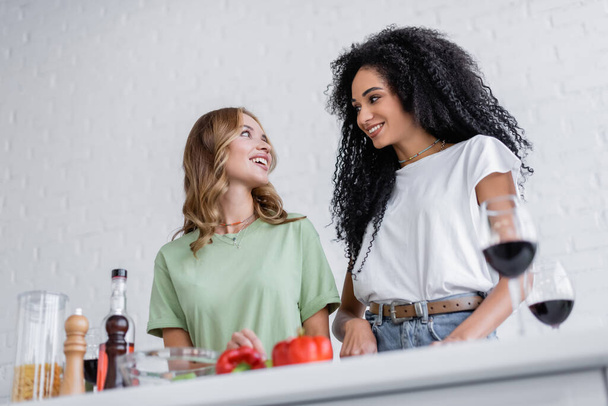 low angle view of happy interracial lesbian couple cooking in kitchen  - Fotografie, Obrázek