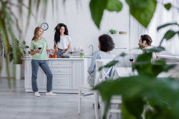 boldog multietnikus barátok beszél a modern konyha homályos növények előtérben  - Fotó, kép