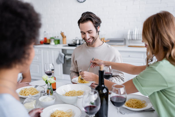 blonde woman serving pasta to cheerful man near blurred african american friend - Photo, Image