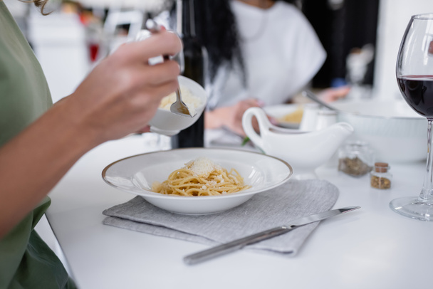 cropped view of woman holding bowl with grated cheese near pasta on plate - Фото, изображение