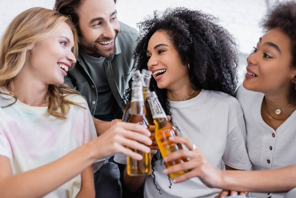 boldog férfi és örömteli fajok közötti nők csörömpölnek üveg sört  - Fotó, kép