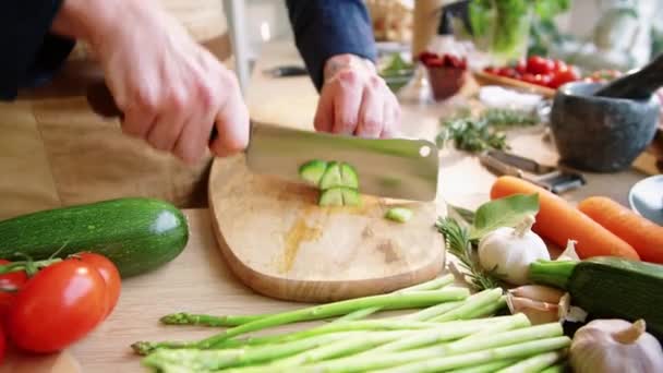Zoom in shot of hands of male chef chopping fresh cucumber on wooden cutting board and the removing pieces from knife blade while cooking in restaurant kitchen - Metraje, vídeo