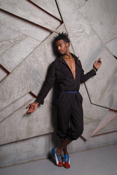 A handsome black man in a stylish jumpsuit against a gray wall. - Foto, immagini