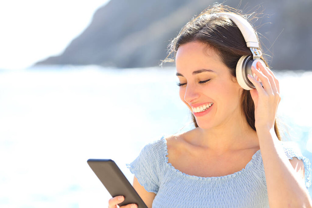 Happy woman listening to music holding headphones and smart phone on summer vacation on the beach - Fotó, kép
