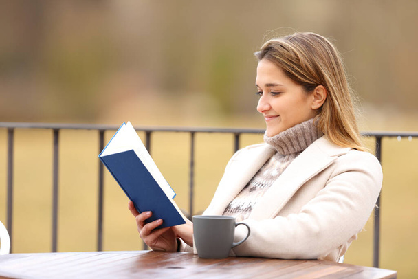 Happy woman reading a book in winter in a terrace - Foto, imagen