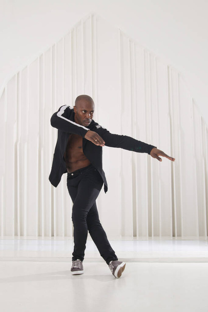 Elegant black man dancer in black clothes is dancing in a bright room. - Photo, image