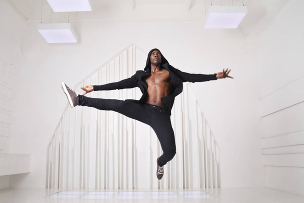 Elegant black man dancer in black clothes jumping in a bright room. - Fotoğraf, Görsel