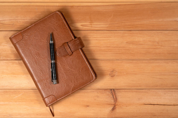 Red color handmade leather notebook cover with notebook and pen inside on wooden background. Stock photo of luxury business accessories. - Foto, afbeelding
