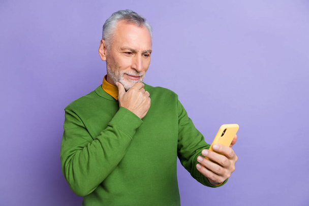 Photo of thoughtful retired man wear green sweater typing modern device isolated violet color background - Foto, imagen