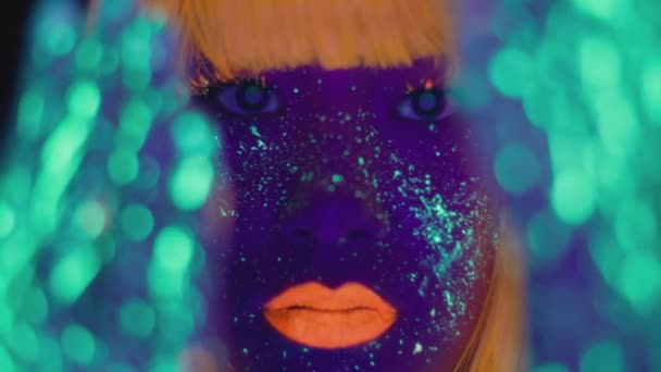 Mladá žena s jasným fluorescenčním make-upem a tělesným uměním pózující na kameru, gestikulující zářícíma rukama, selektivní zaměření - Záběry, video