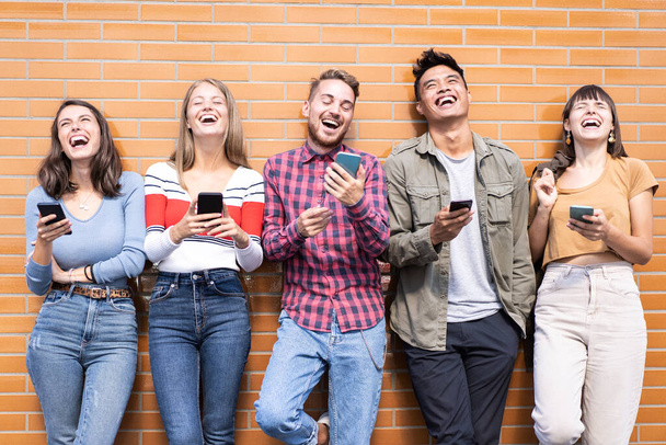 Gruppe fröhlicher Freunde amüsiert sich im Freien mit Mobiltelefonen - Junge Leute lachen in der Pause im Uni-Hinterhof gemeinsam - Gesichter im Fokus - Foto, Bild