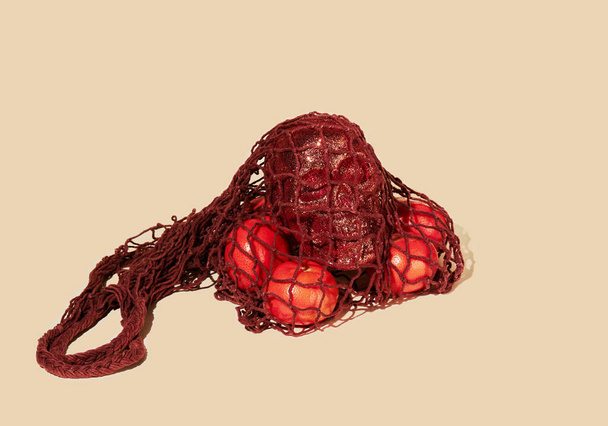 ベージュ地の茶色のストリングバッグ(メッシュエコバッグ、ニットラグバッグ)にタンジェリンと輝く人間の頭蓋骨。現代の再利用可能なショッピング、廃棄物のないコンセプト - 写真・画像
