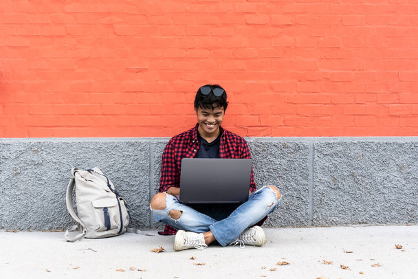 Digitale Nomaden und Technologie Job überall Konzept mit jungen Mann sitzen im Freien arbeiten oder studieren mit Laptop in einem alternativen kostenlosen Büro oder im Hinterhof der Universität - Foto, Bild