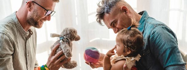 Vaaka banneri tai otsikko mies homo pari hyväksyi vauva tyttö kotona kaksi isää leikkii tyttärensä Lgbtq + perhe kotona monimuotoisuus käsite ja LGBTQ perhesuhde - Valokuva, kuva