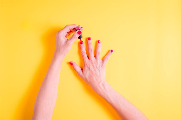 Sarı arka plana kırmızı oje sürerken kadınların elleri - Fotoğraf, Görsel