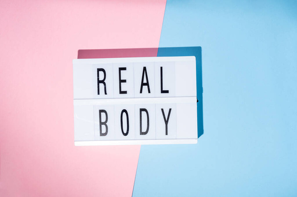 Texte Real Body sur la lightbox. Concept de féminisme sur fond bleu et rose. Vue du dessus - Photo, image