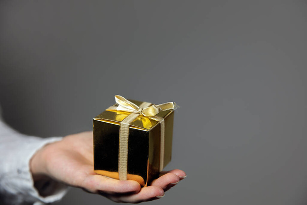 Mains tenant boîte cadeau en or isolé sur fond gris. donnant cadeau, Anniversaire, Noël, Fête des mères autre Vacances avec espace de copie pour le texte - Photo, image
