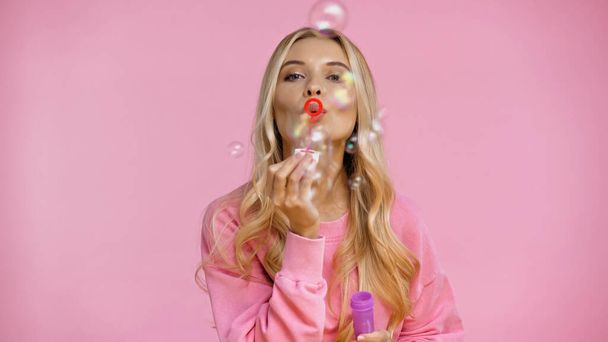 Blonde woman blowing soap bubbles isolated on pink  - Foto, Imagen