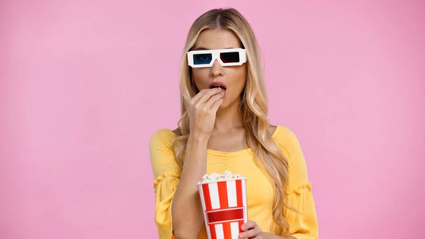 Blonde woman in 3d glasses eating popcorn isolated on pink  - Photo, Image
