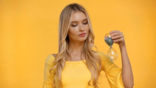 Blonde woman in blouse holding hourglass isolated on yellow  - Φωτογραφία, εικόνα