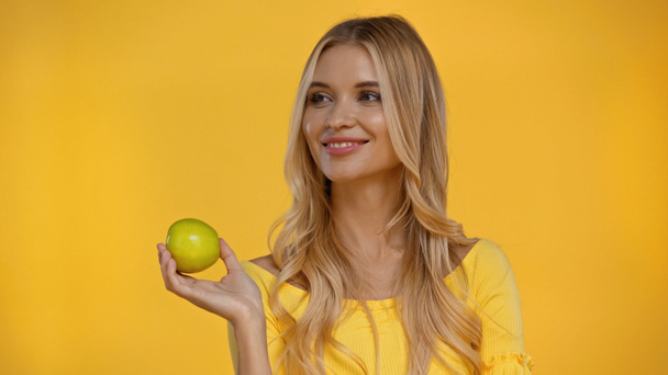 Cheerful woman holding fresh green apple isolated on yellow  - Фото, изображение