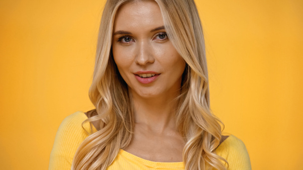Hübsche blonde Frau in Bluse blickt vereinzelt in die Kamera auf gelb  - Foto, Bild