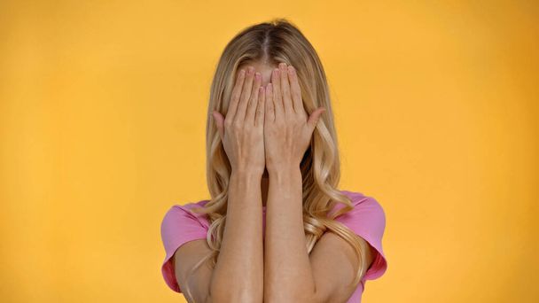 Blonde woman in t-shirt covering face with hands isolated on yellow  - Foto, immagini