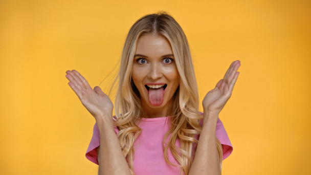 Blonde woman sticking out tongue and looking at camera isolated on yellow  - Фото, зображення