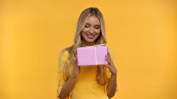 Pretty blonde woman holding present isolated on yellow  - Фото, изображение