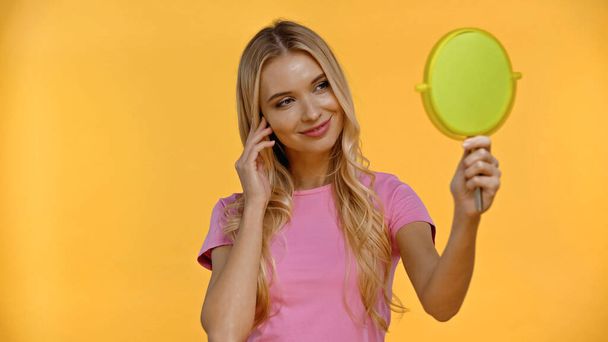 Smiling blonde woman holding mirror isolated on yellow  - Fotografie, Obrázek