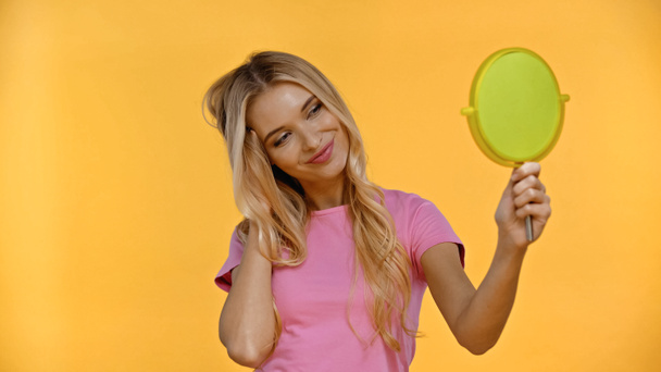 Pretty blonde woman smiling while holding mirror isolated on yellow  - Φωτογραφία, εικόνα