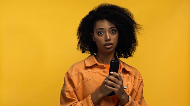 donna afro-americana scioccata con telecomando isolato su giallo - Foto, immagini