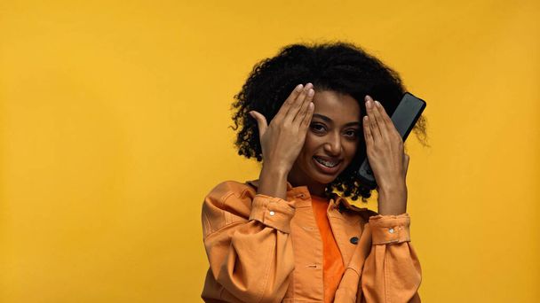 黄色に隔離されたリモコンを持っているブレースを持つ陽気なアフリカ系アメリカ人女性 - 写真・画像