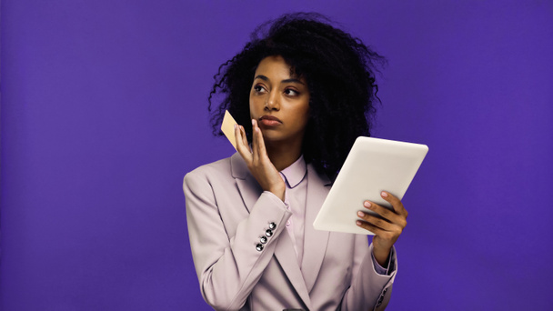 joven afroamericana mujer en chaqueta sosteniendo tableta digital y tarjeta de crédito aislado en púrpura  - Foto, imagen