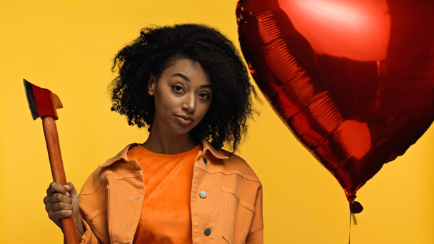 Afrikaans-Amerikaanse vrouw houdt hamer in de buurt van rode hartvormige ballon geïsoleerd op geel, Valentijnsdag concept  - Foto, afbeelding