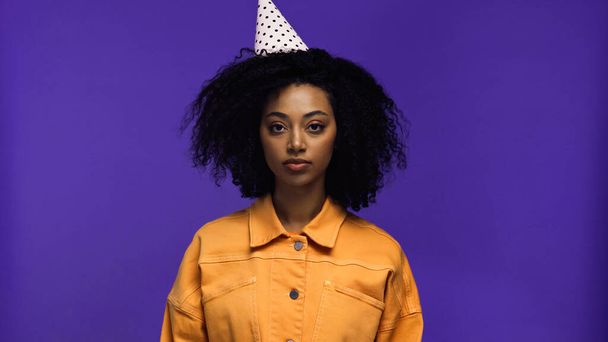 young african american woman in party cap looking at camera isolated on purple - Φωτογραφία, εικόνα
