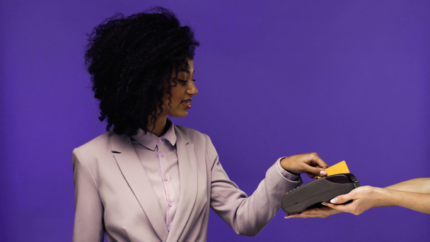 усміхнена афроамериканська бізнес-леді в брекетах, що платять кредитною карткою ізольовано на фіолетовому
  - Фото, зображення