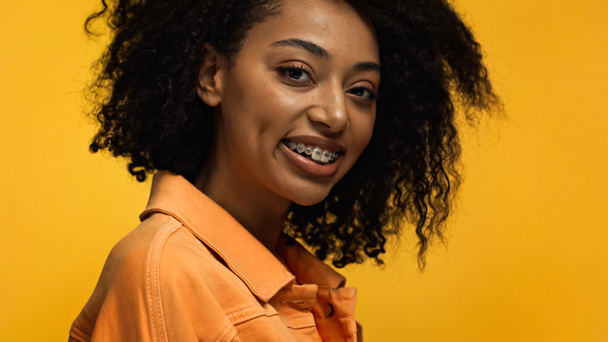 Χαρούμενη Αφροαμερικανή γυναίκα με σιδεράκια χαμογελώντας απομονωμένη στο κίτρινο - Φωτογραφία, εικόνα