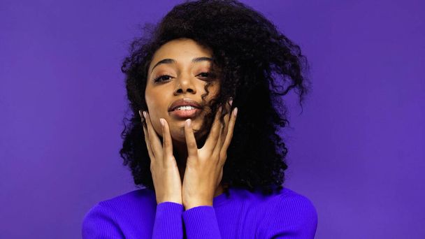 young african american woman with braces touching face isolated on purple  - Foto, Imagem